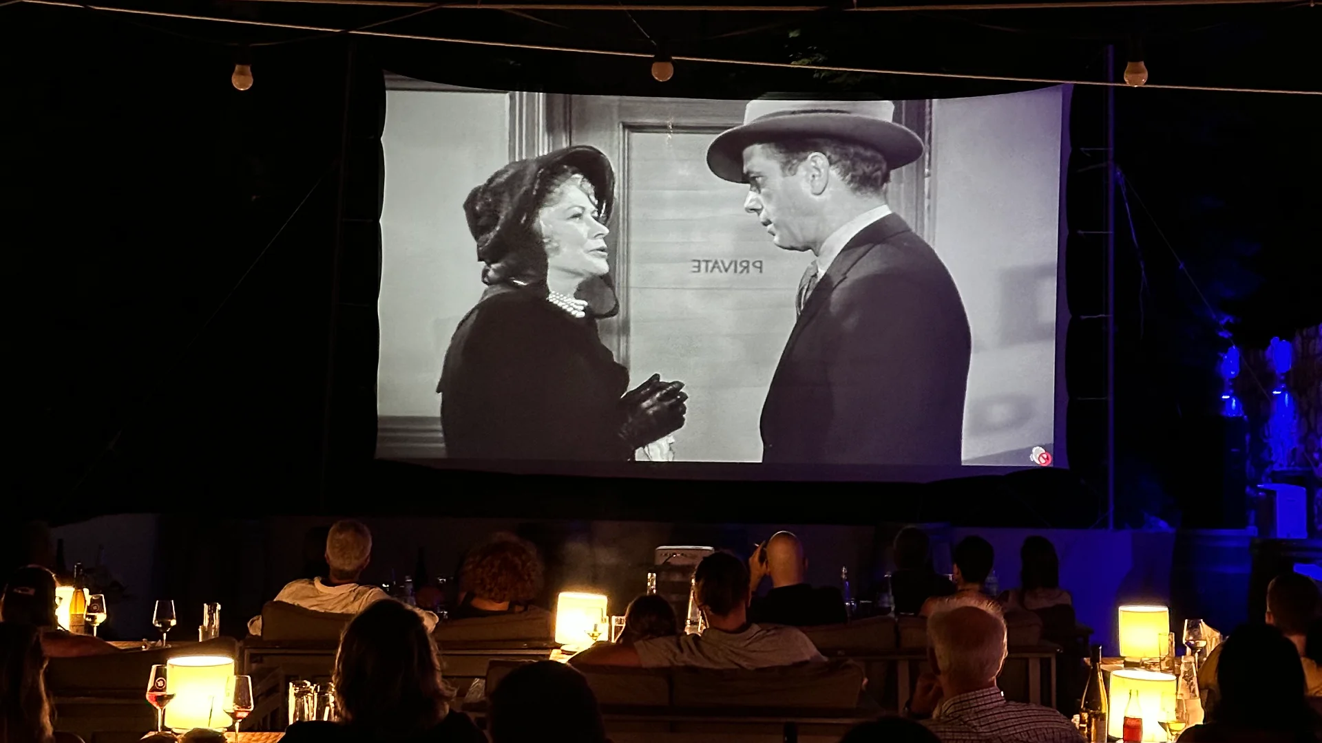 TherOina at night: a classic film on the big screen, guests on the couches by lamplight